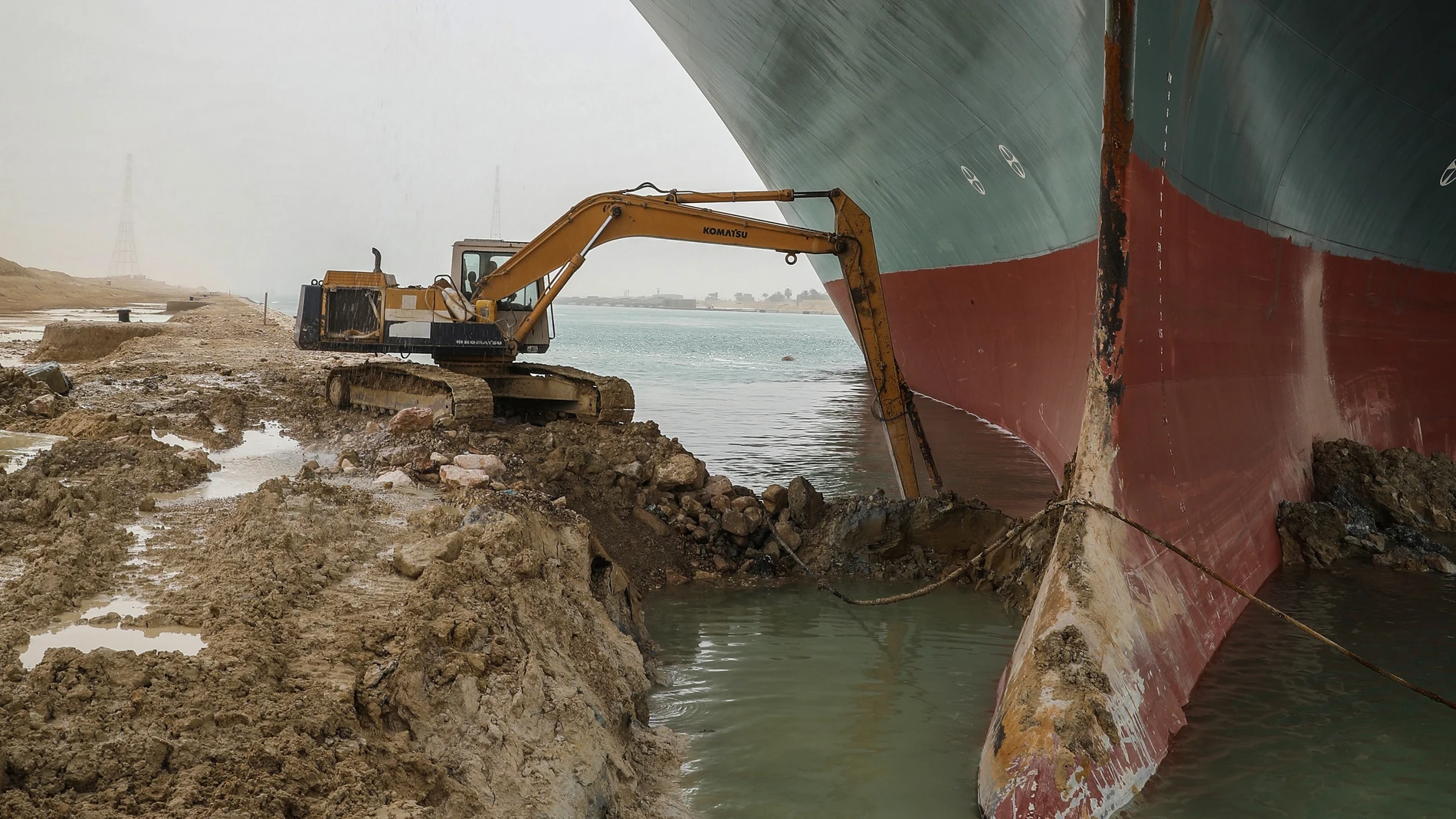 Una excavadora trata de retirar arena de la orilla para desencallar al carguero Ever Given