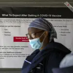 Una sanitaria pasa por un cartel en el que se informa de posibles efectos secundarios de la vacuna en Johannesburgo (Suráfrica)