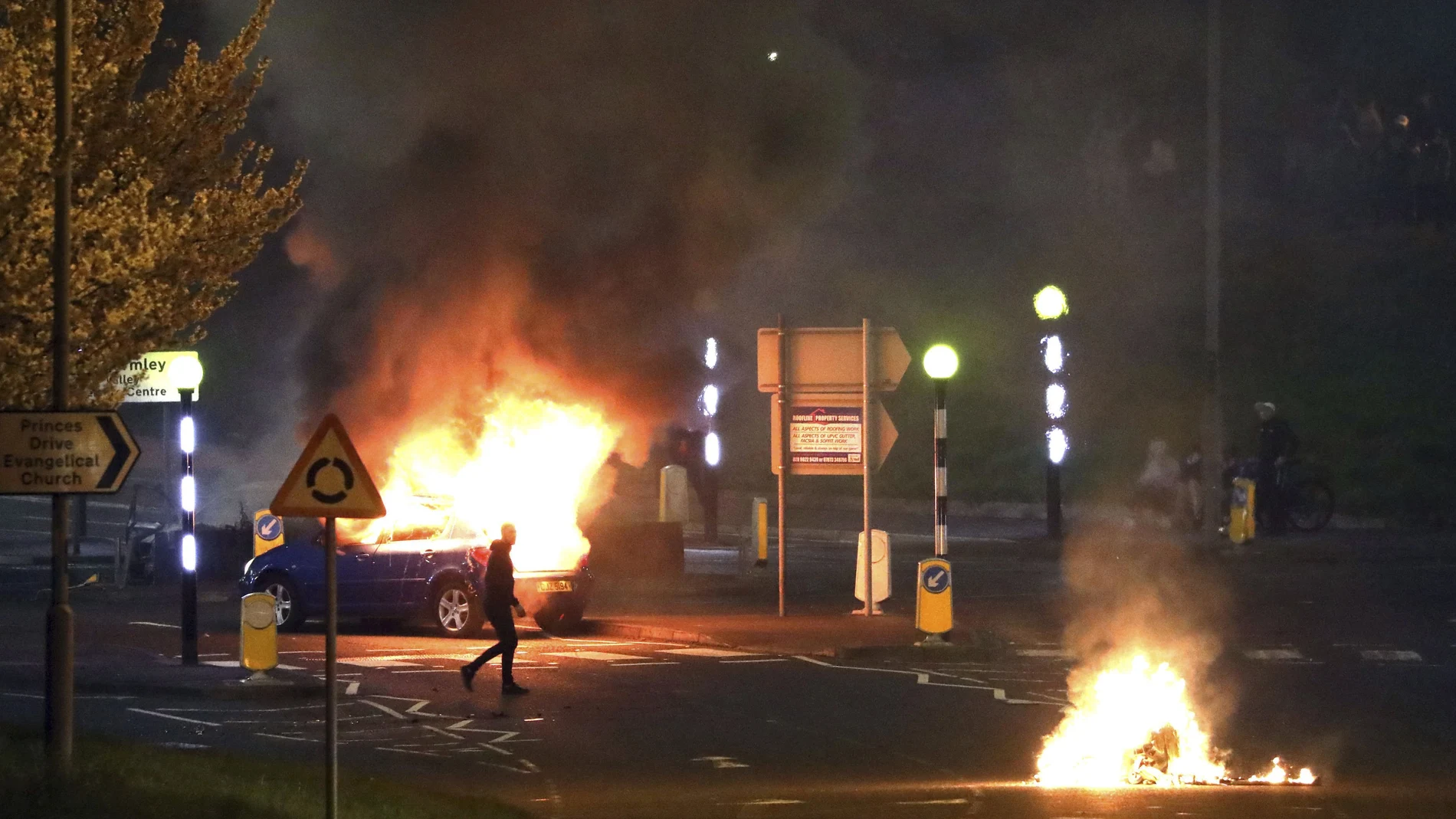 Un hombre pasa junto a un coche incendiado en Belfast la noche del sábado