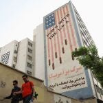 Iraníes caminan por Teherán con el mural antiamericano de fondo el día en el que se ha reanudado el diálogo nuclear