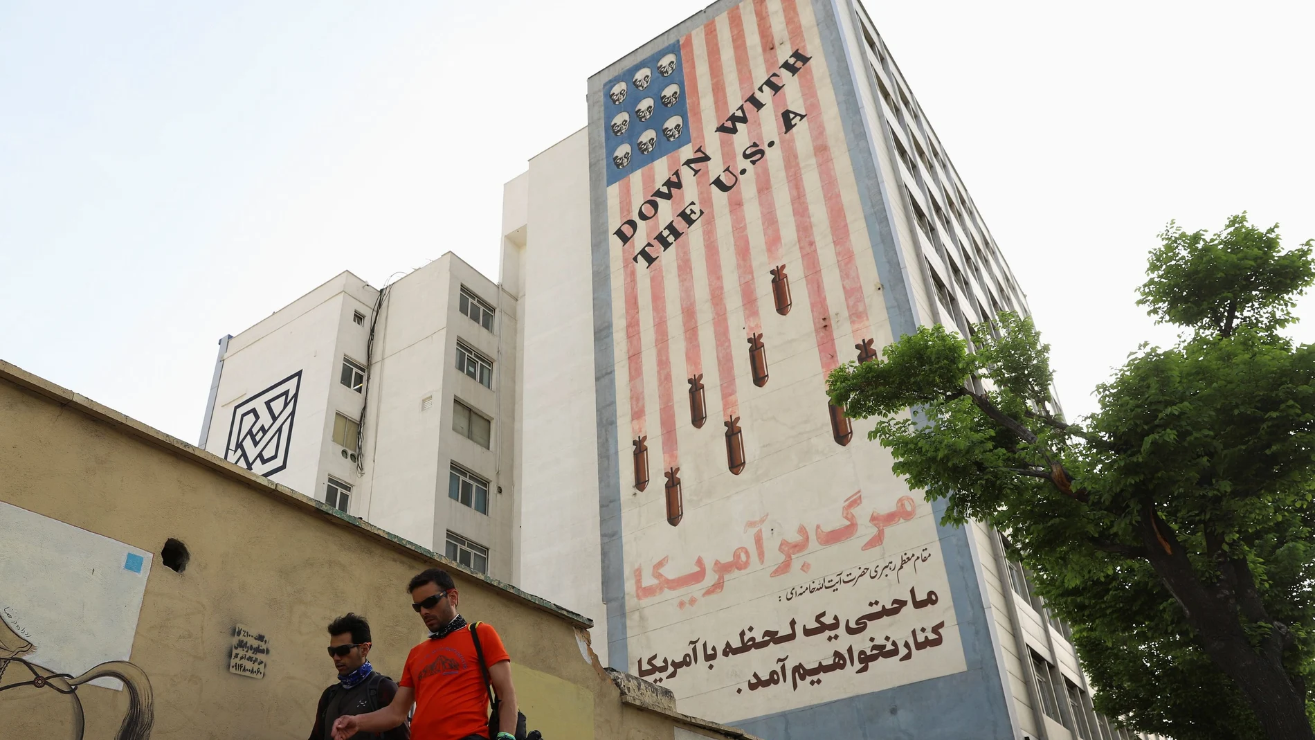 Iraníes caminan por Teherán con el mural antiamericano de fondo el día en el que se ha reanudado el diálogo nuclear
