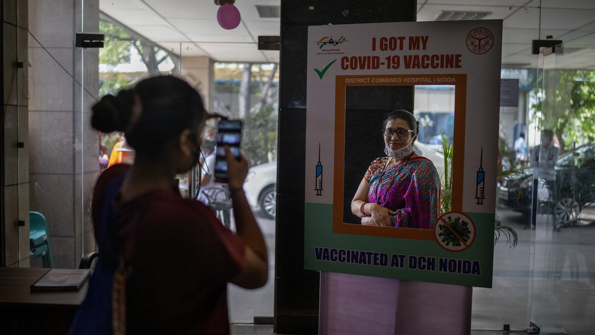 A woman poses for a photograph behind a cutout after receiving a COVID- 19 vaccine at a government hospital in Noida, a suburb of New Delhi, India, Wednesday, April 7, 2021. India hits another new peak with 115,736 coronavirus cases reported in the past 24 hours with New Delhi, Mumbai and dozens of other cities imposing night curfews to check the soaring infections. (AP Photo/Altaf Qadri)