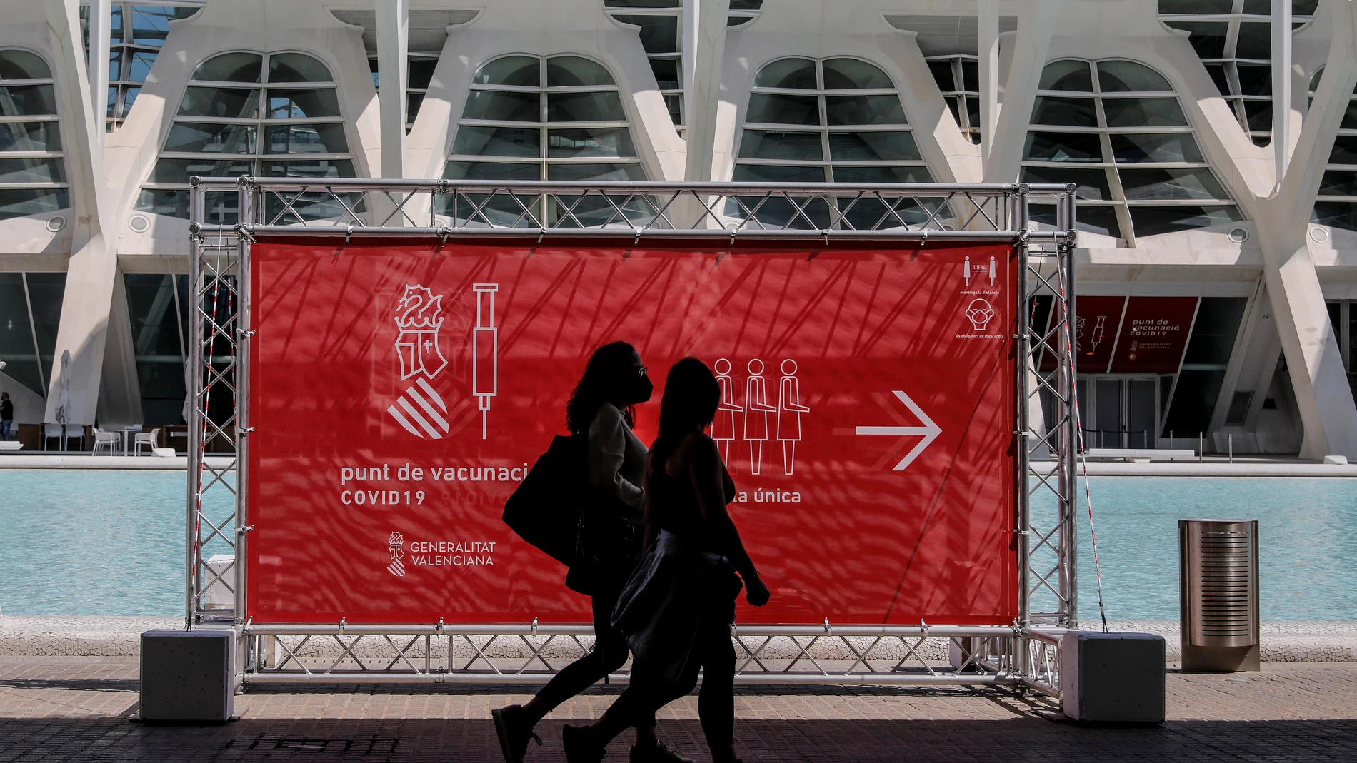 Dos personas pasan por un cartel que indica el punto de vacunación de la Ciudad de las Artes y las Ciencias de Valencia