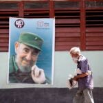 Un hombre con mascarilla camina frente a una imagen de Fidel Castro en una calle de La Habana (Cuba)