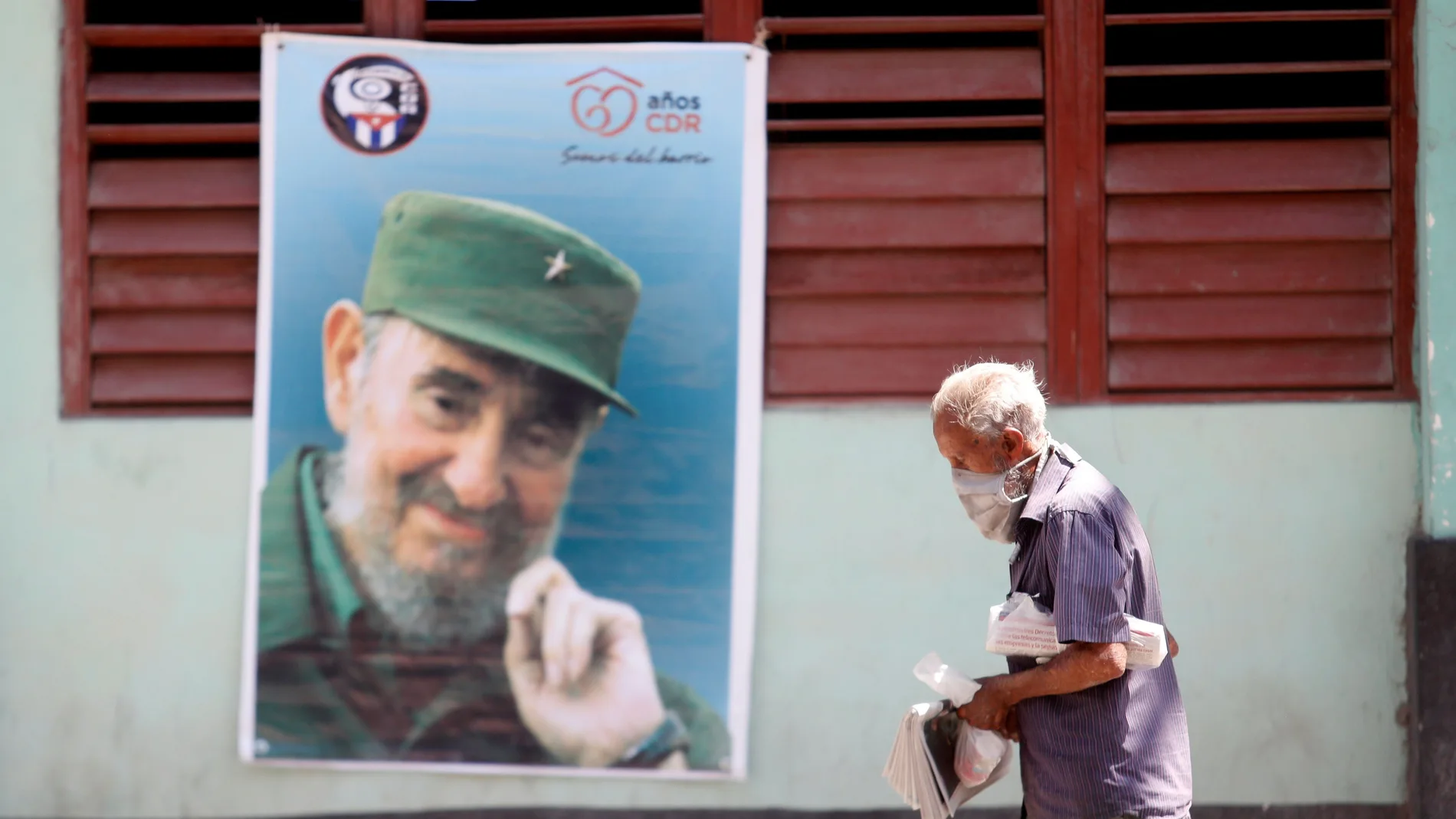 Un hombre con mascarilla camina frente a una imagen de Fidel Castro en una calle de La Habana (Cuba)