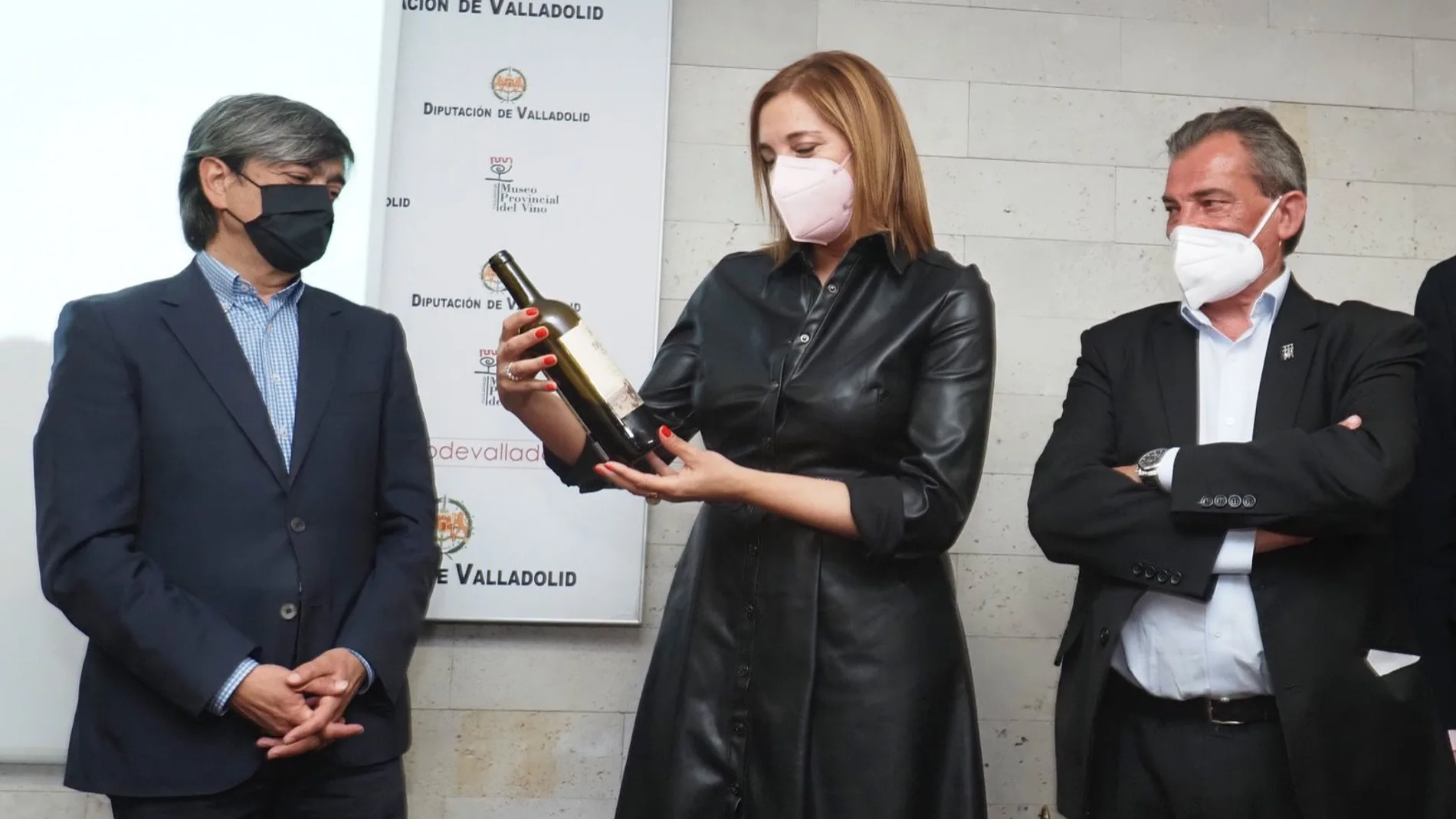 La presidenta de Sodeva, Inmaculada Toledano, sujeta una botella del Vino Museo en presencia del diputado provincial, Agapito Hernández, , y del presidente de los sumilleres de España, Pablo Martín