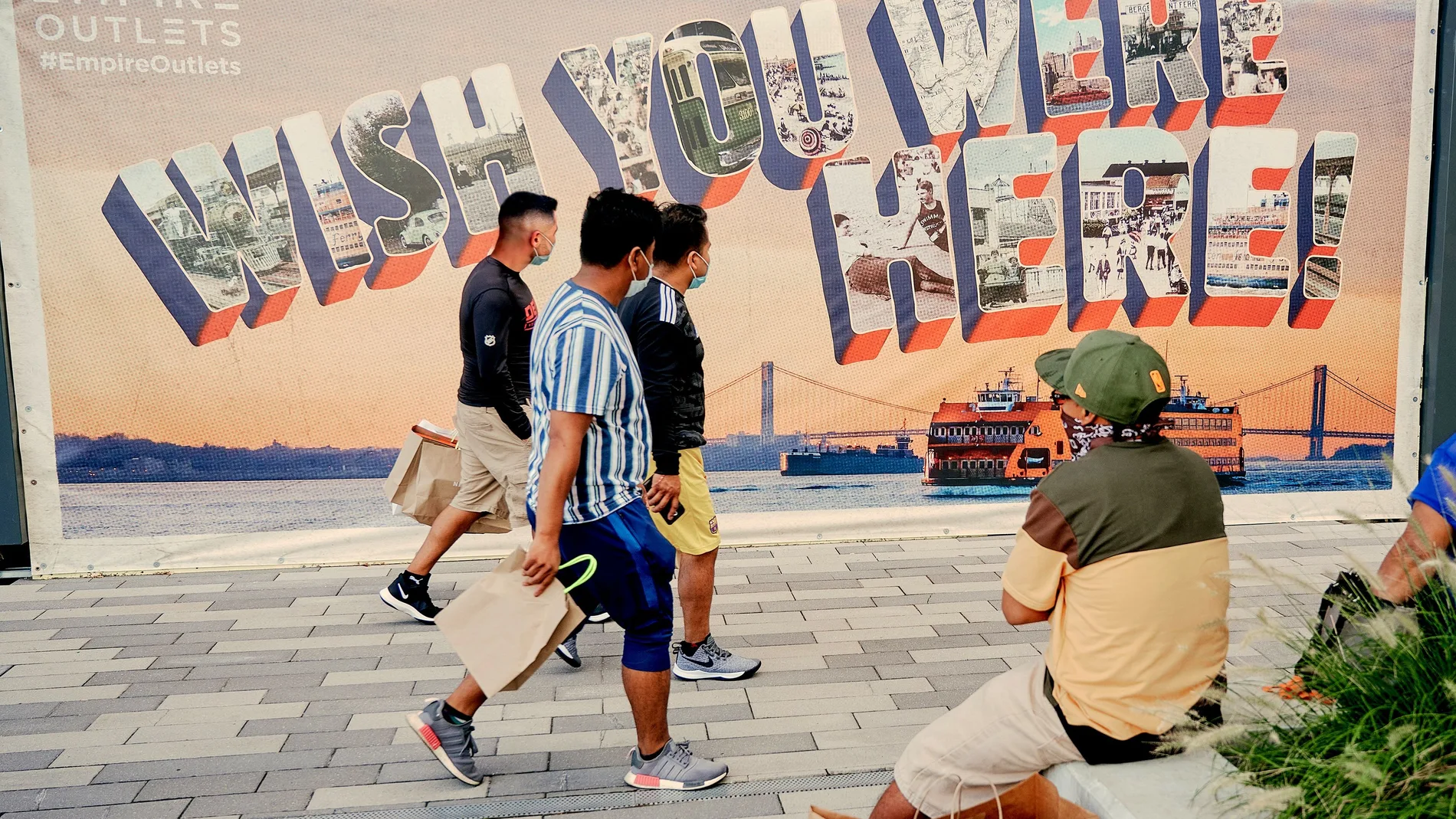 Fotografía cedida por NYC & Company, oficina de promoción turística de Nueva York, donde aparecen unas personas mientras caminan frente a un mural pintado con la icónica tarjeta postal que dice "Wish you were here"