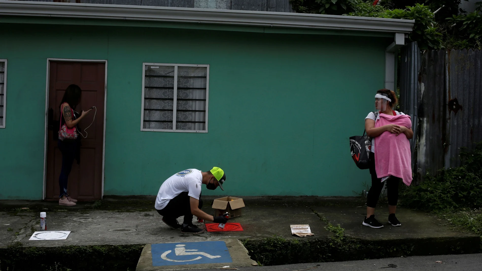 FILE PHOTO: A worker sprays paint on a stencil indicating social distancing on the floor of a bus stop, as the spread of the coronavirus disease (COVID-19) continues, in San Jose, Costa Rica July 24, 2020. REUTERS/Juan Carlos Ulate/File Photo