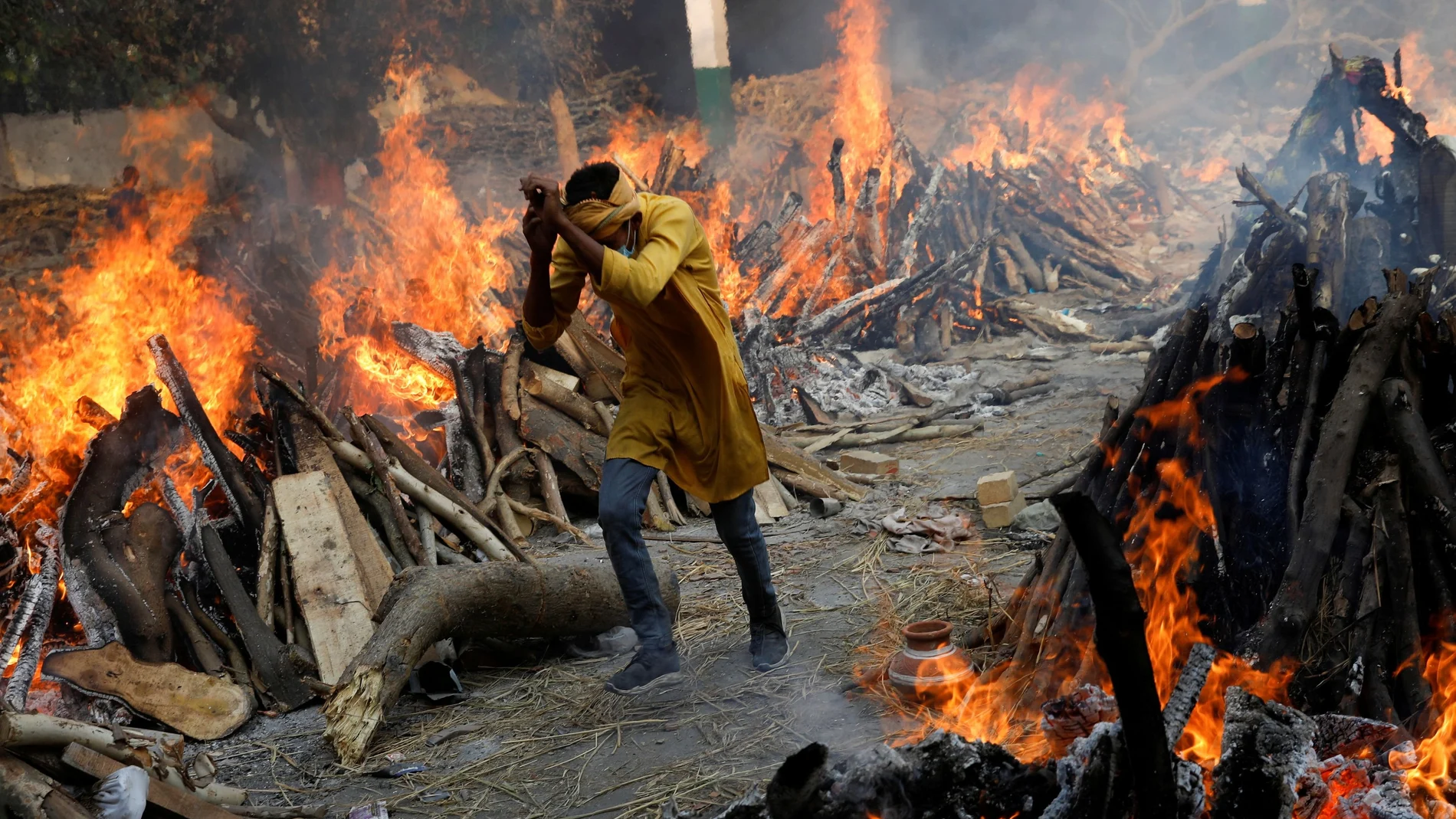 Un hombre pasa corriendo junto a las piras funerarias en llamas durante una cremación masiva en Nueva Delhi (India).
