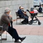 Varias personas mayores descansa sentadas en bancos en la calle