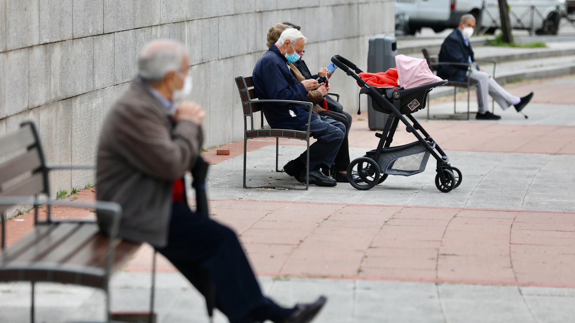 Varias personas mayores descansa sentadas en bancos en la calle