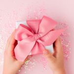 Manos de un niño que sostienen un regalo con lazo rosa