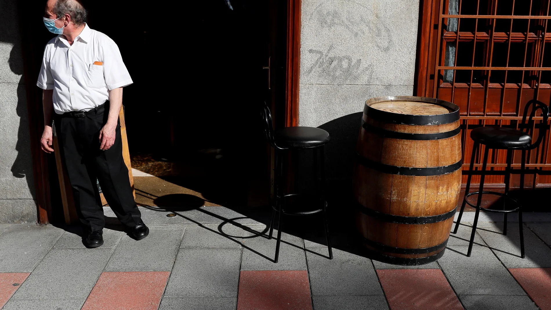 Un camarero espera la llegada de clientes a las puertas de un restaurante