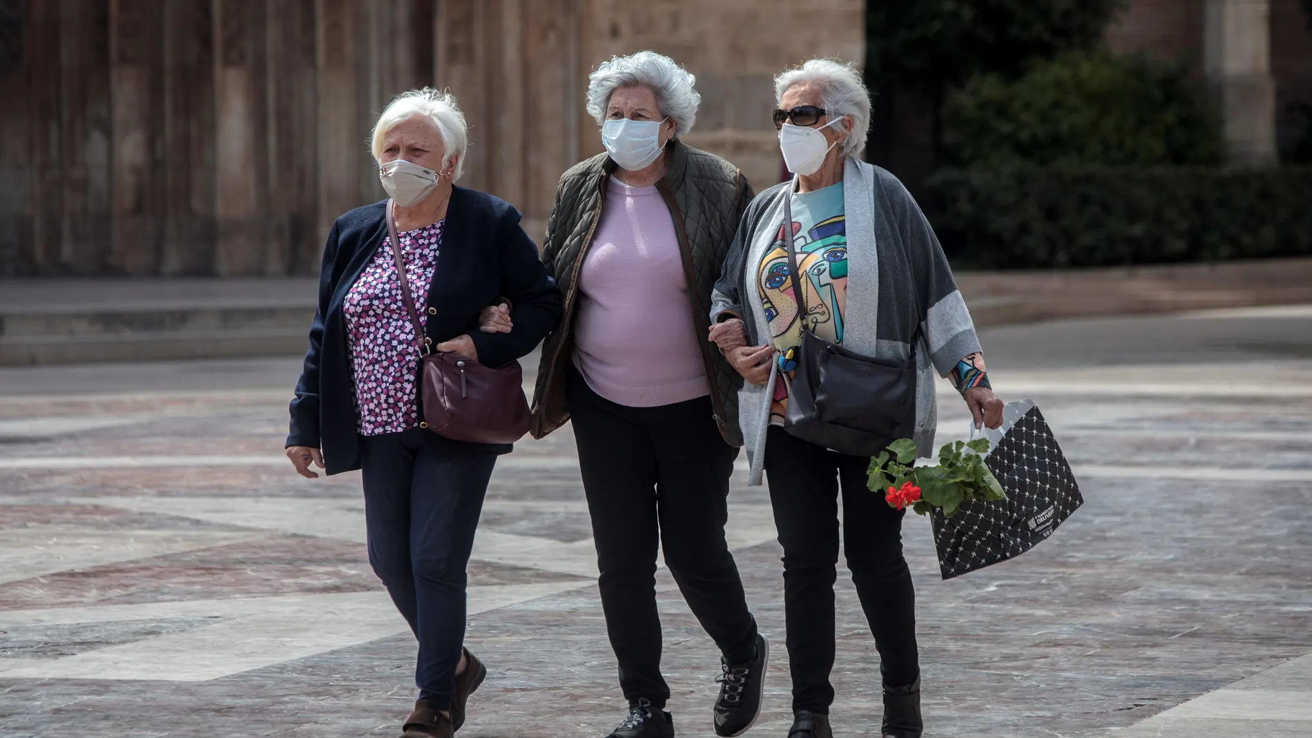 Tres señoras caminan cogidas del brazo en una céntrica plaza de Valencia