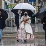 Una fallera se dirige a la Basílica de Valencia con un paraguas y un ramo de flores para la Virgen de los Desamparados, en Valencia, Comunidad Valenciana (España), a 18 de marzo de 2021