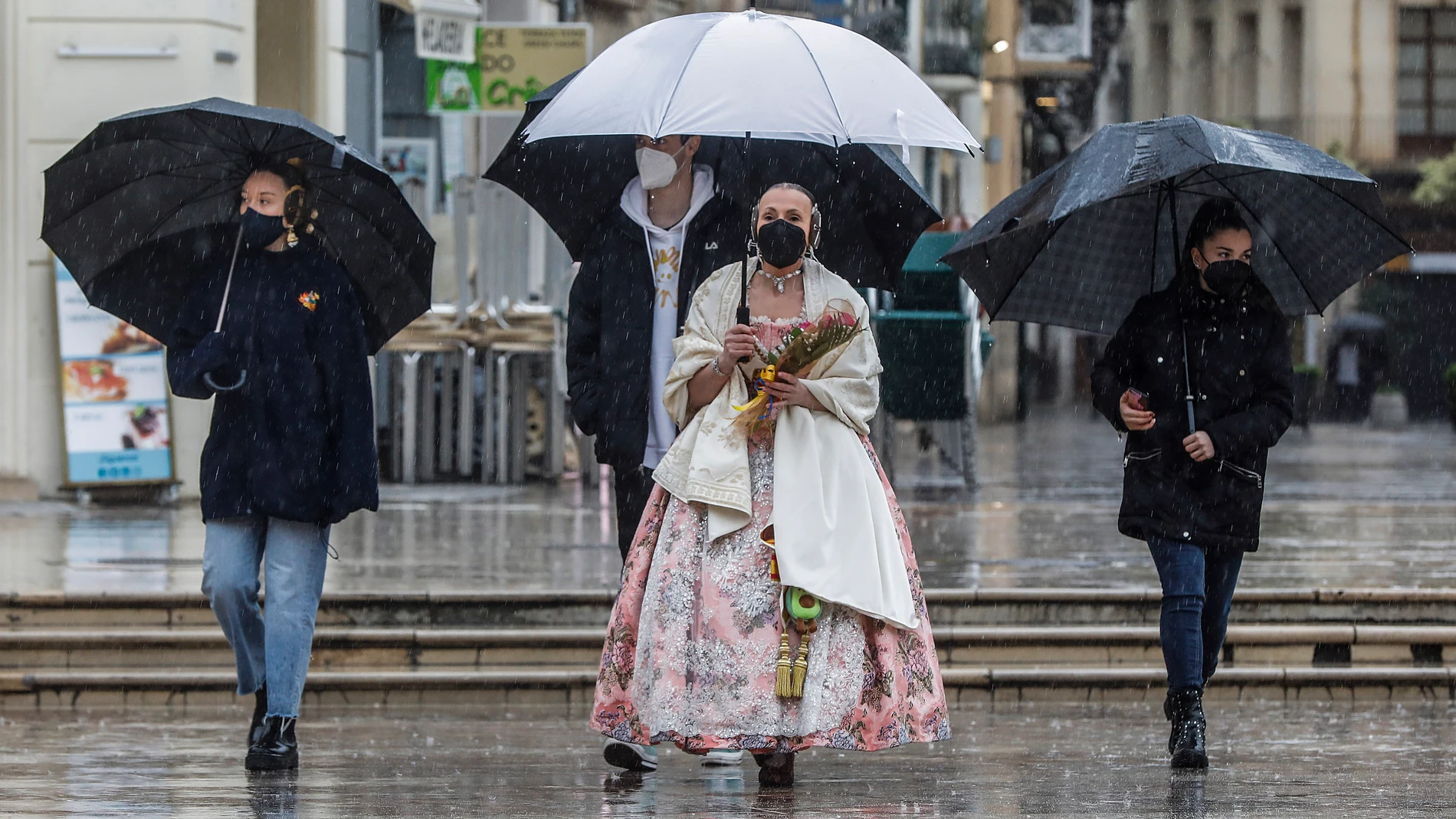 Una fallera se dirige a la Basílica de Valencia con un paraguas y un ramo de flores para la Virgen de los Desamparados, en Valencia, Comunidad Valenciana (España), a 18 de marzo de 2021