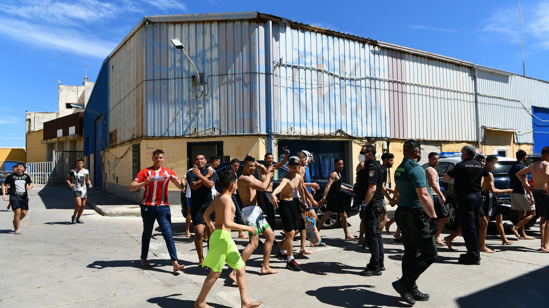 Un grupo de jóvenes migrantes marroquíes en fila en las inmediaciones de una nave, a 17 de mayo de 2021, en Ceuta (España). La delegación ha cifrado que unas 1000 personas, de las que al menos 300 son menores de edad, han conseguido sortear los espigones que separan los dos lados de las frontera, tanto en la bahía sur, en el paso del Tarajal y en la bahía norte, en la playa de Benzú. La guardia civil los ha trasladado en grupos hasta las naves del polígono industrial donde tiene el dispositivo de acogida de migrantes para hacer cumplir los protocolos sanitarios para evitar contagios de COVID 19.17 MAYO 2021;INMIGRACION;CEUTA;VALLA;ESTRECHO;MARROQUIESAntonio Sempere / Europa Press17/05/2021