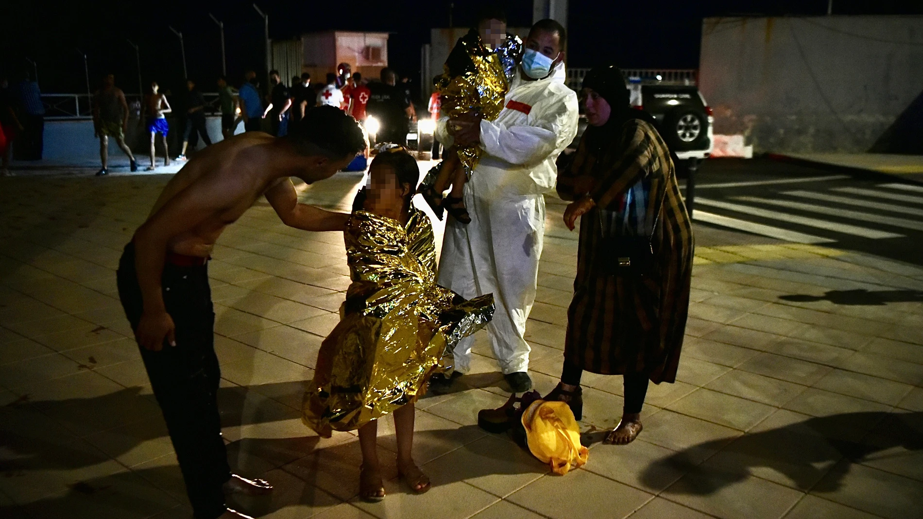 Un hombre migrante coge en brazos a un menor acompañado de una mujer y una niña pequeña, en Ceuta