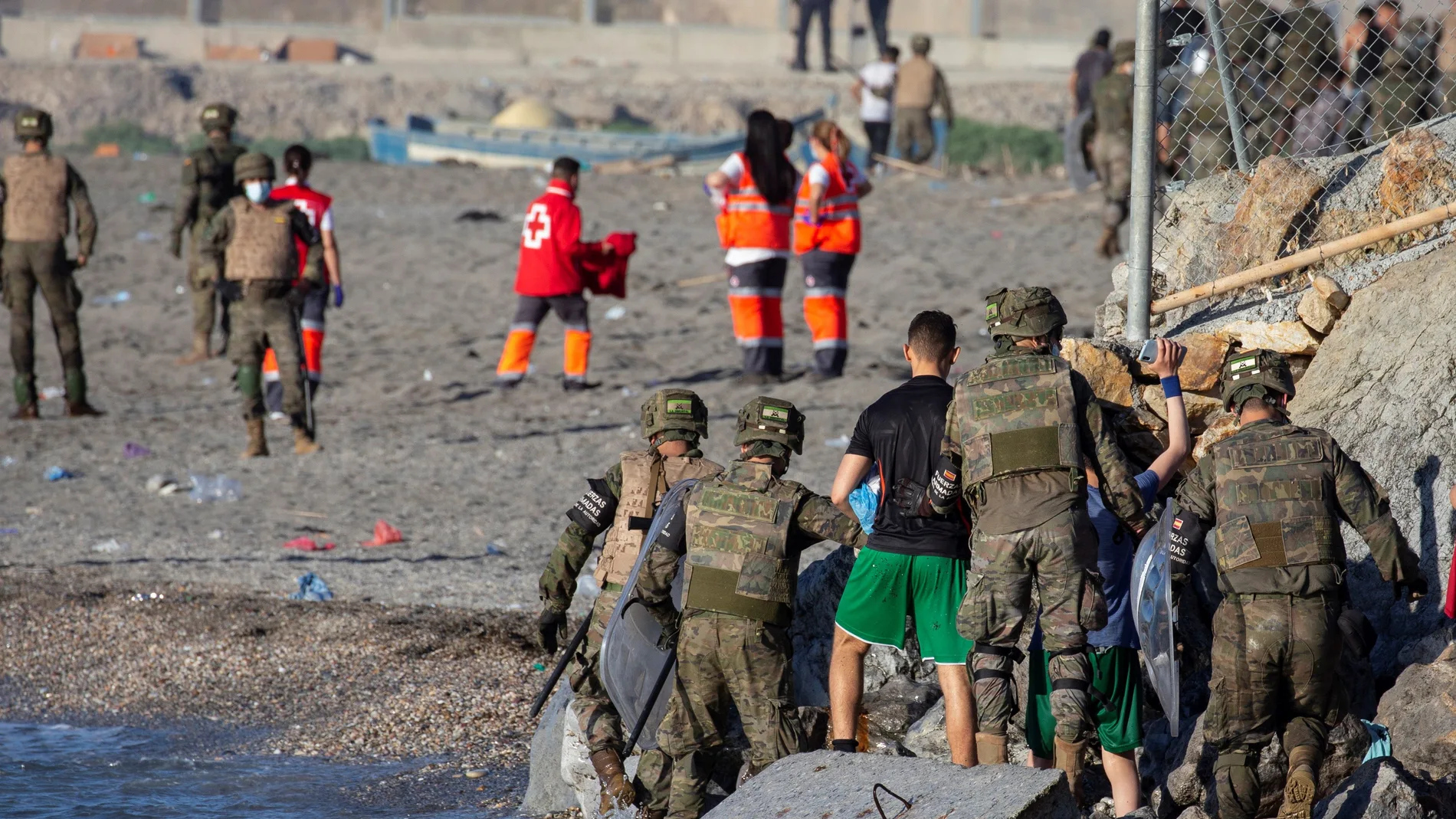 Miembros del ejército ayudando a varios inmigrantes a su llegada a la playa de El Tarajal, junto a la valla fronteriza , en Ceuta.