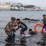 Un soldado del Ejército español ayuda a dos migrantes a salir del agua en la playa de El Tarajal