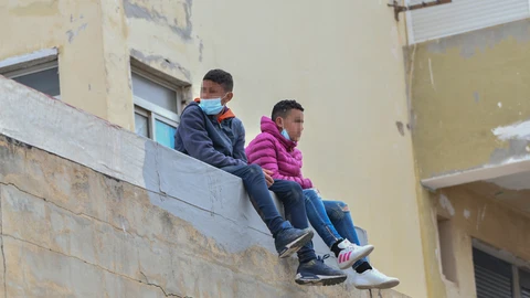 Dos niños sentados sobre un muro en la nave de primera acogida del polígono del Tarajal