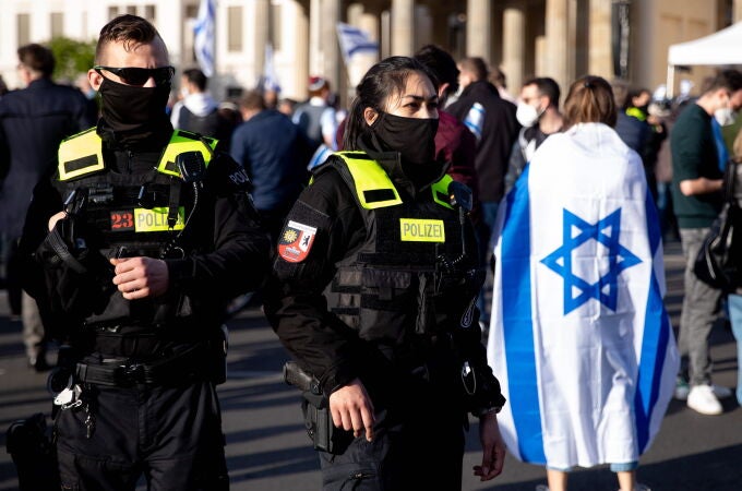 Una mujer con bandera de Israel junto a agentes de policía asiste a un mitin denominado 'Solidaridad con Israel y contra el antisemitismo' frente a la Puerta de Brandenburgo en Berlín, Alemania, el 20 de mayo