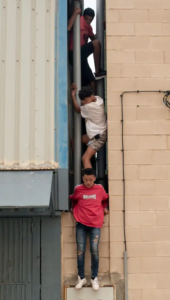 Tres migrantes se escapan de la nave del polígono industrial cercano a la playa de El Tarajal en donde permanecían gran parte de los menores migrantes llegados a Ceuta. EFE/ Brais Lorenzo