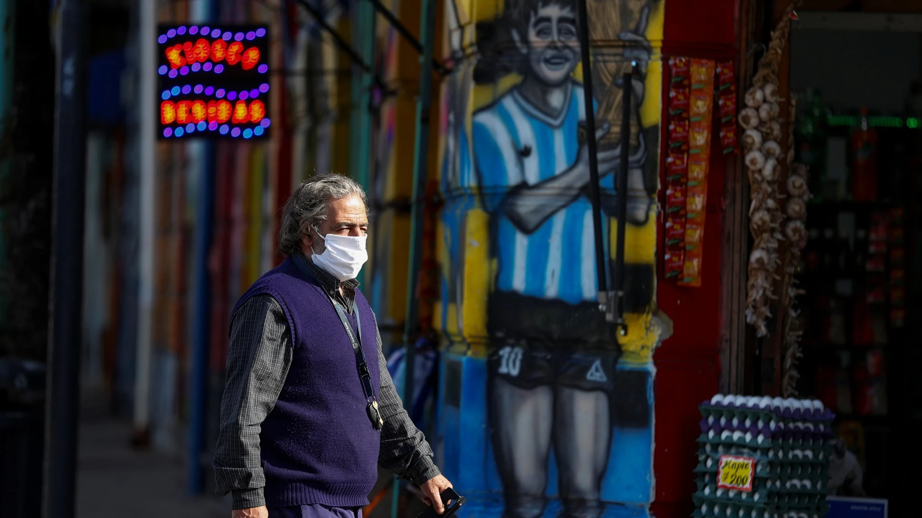 A man wearing a face mask as a preventive measure against the coronavirus disease (COVID-19) walks past a grocery store painted with a graffiti depicting Diego Maradona, after CONMEBOL announced Argentina pulled out hosting the Copa America, in Buenos Aires, Argentina May 31, 2021. REUTERS/Agustin Marcarian