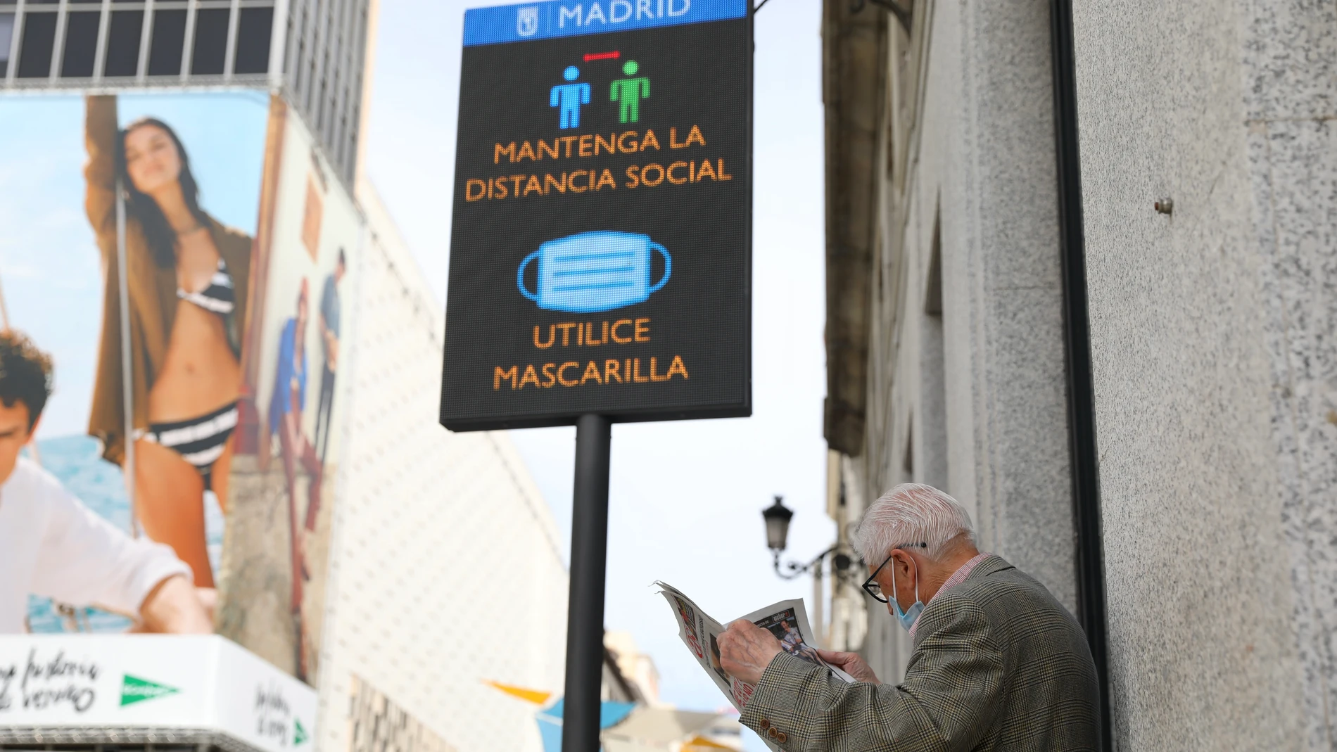 Un jubilado lee el periódico en una calle comercial madrileña