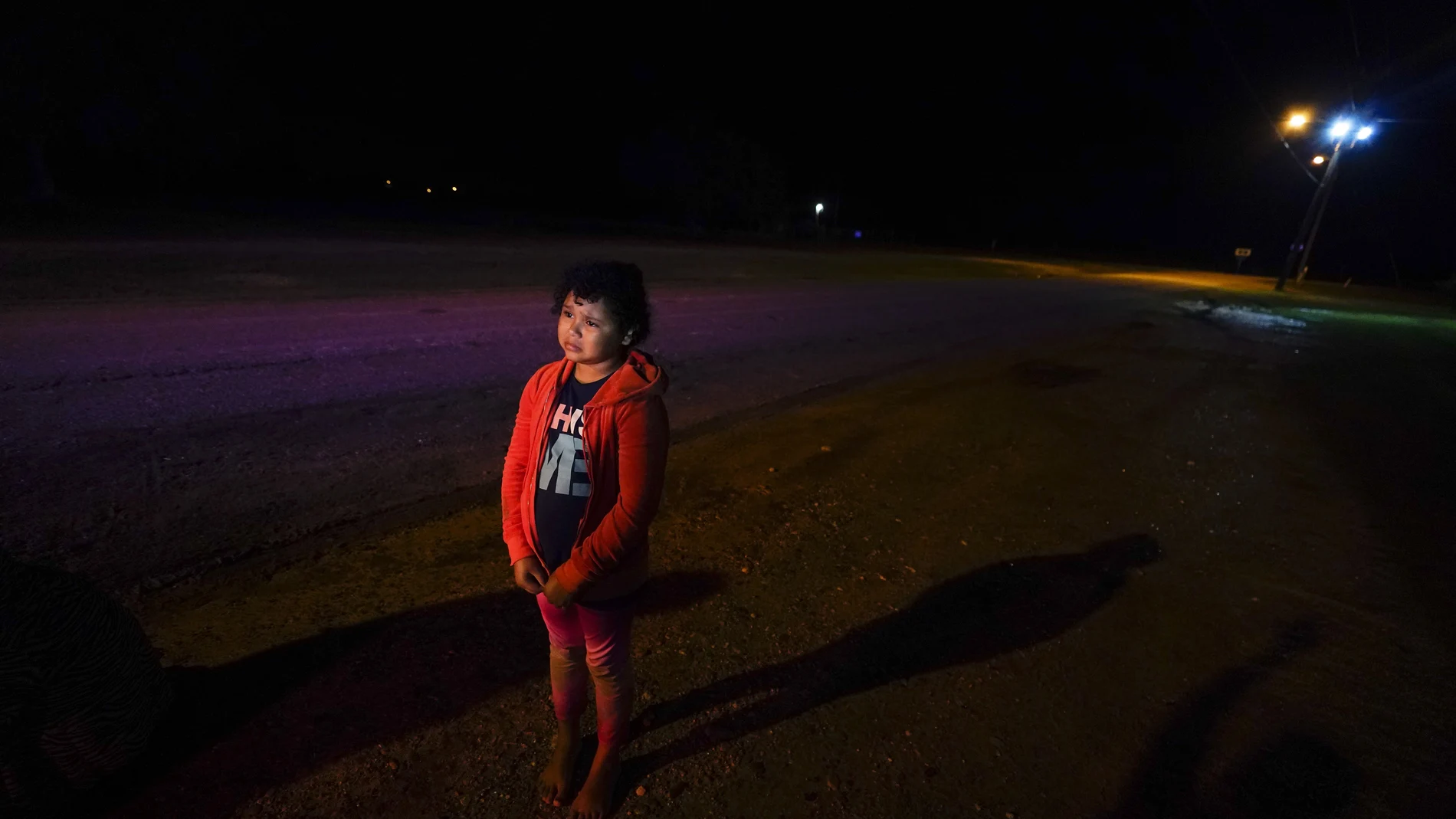 FILE - In this May 13, 2021, file photo, Emely, 8, of Honduras, stands alone after turning herself in upon crossing the U.S.-Mexico border in La Joya, Texas. Her mother, Glenda Valdez was at her home in Austin, watching a Univision newscast one afternoon in May, when she saw this picture of Emely in a red hoodie. She knew at once that it was her daughter. Desperate, she immediately began making calls to U.S. authorities, the network and refugee agencies. (AP Photo/Gregory Bull, File)