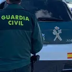 Un agente de la Guardia Civil de espaldas y junto a un vehículo oficial del cuerpo
