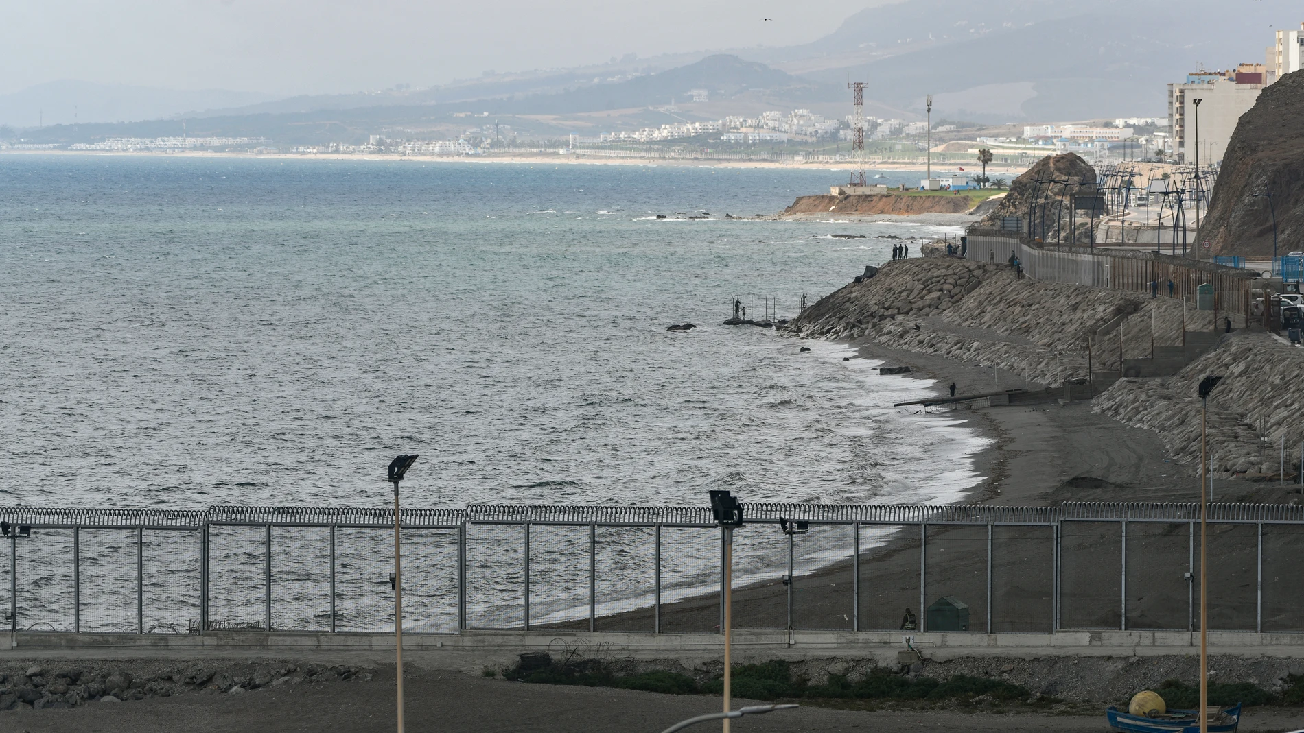 Personas (al fondo), instalan una valla en la playa del Tarajal, a 24 de junio de 2021, en Marruecos
