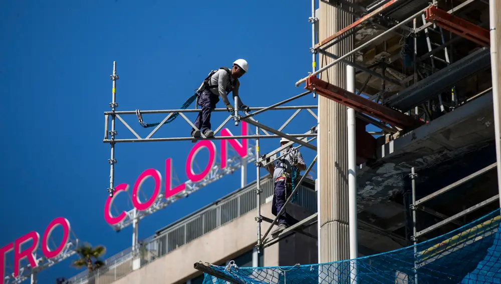 Imagen de unos operarios desmontando andamios en la Torre Colon con la letras del edificio Centro Colon a la espalda.