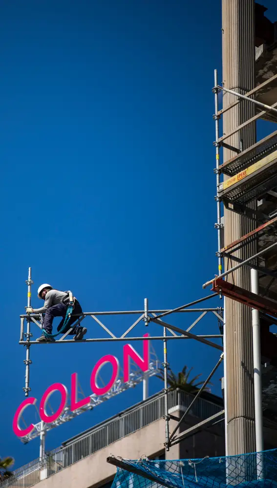 Imagen de unos operarios desmontando andamios en la Torre Colon con la letras del edificio Centro Colon a la espalda. AAA.