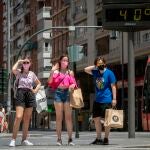 Tres mujeres esperan para cruzar un paso de peatones junto a un termómetro
