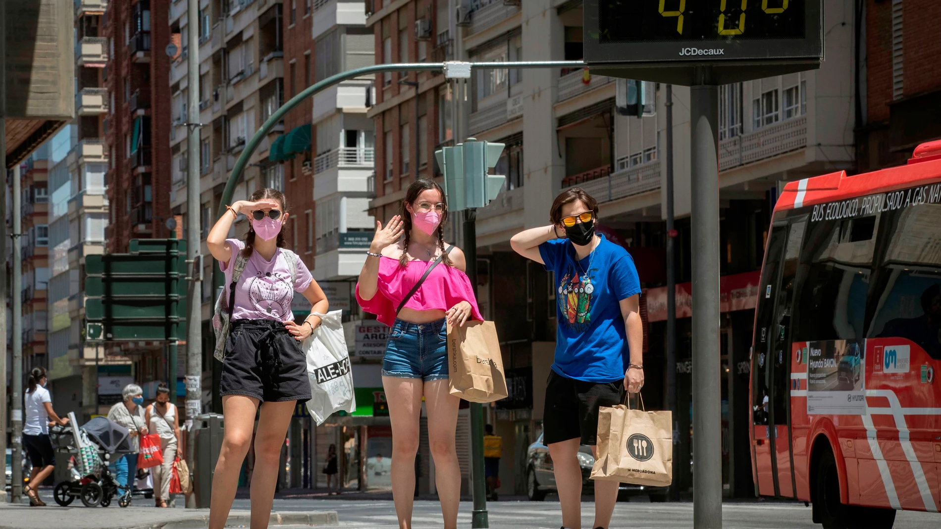 Tres mujeres esperan para cruzar un paso de peatones junto a un termómetro