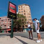 Dos jóvenes beben agua junto a un termómetro que marca 43 grados centígrados, este martes en la Plaza del Royo de Murcia