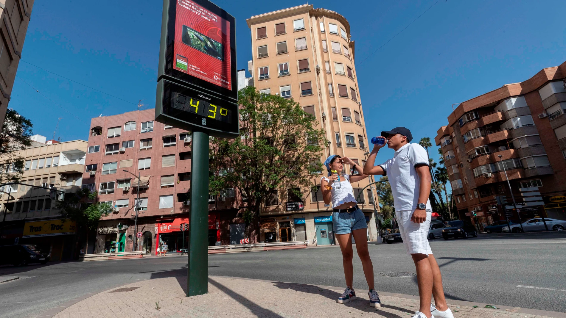 Dos jóvenes beben agua junto a un termómetro que marca 43 grados centígrados, este martes en la Plaza del Royo de Murcia