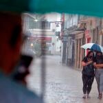 Dos mujeres tratan de protegerse, este lunes, de la intensa lluvia que caía esta mañana en el centro de la ciudad de Gandía. Según la Agencia Estatal de Meteorología (Aemet), la situación meteorológica a las 9 de esta mañana era de tormentas casi generalizadas en la provincia de Valencia, de intensidad fuerte y localmente muy fuerte.