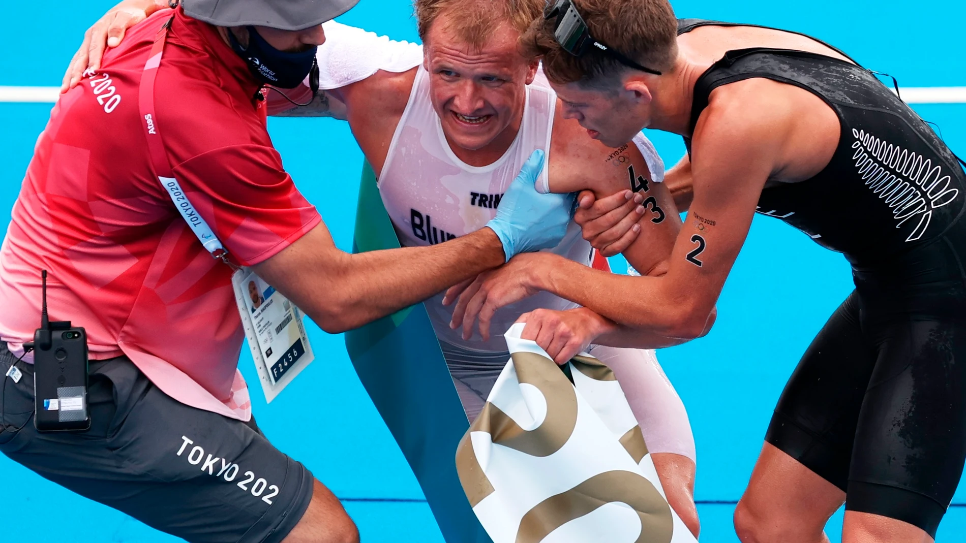 Kristian Blummenfelt es ayudado, después de proclamarse campeón olímpico de triatlón, por un voluntario y por Hayden Wilde, que fue tercero