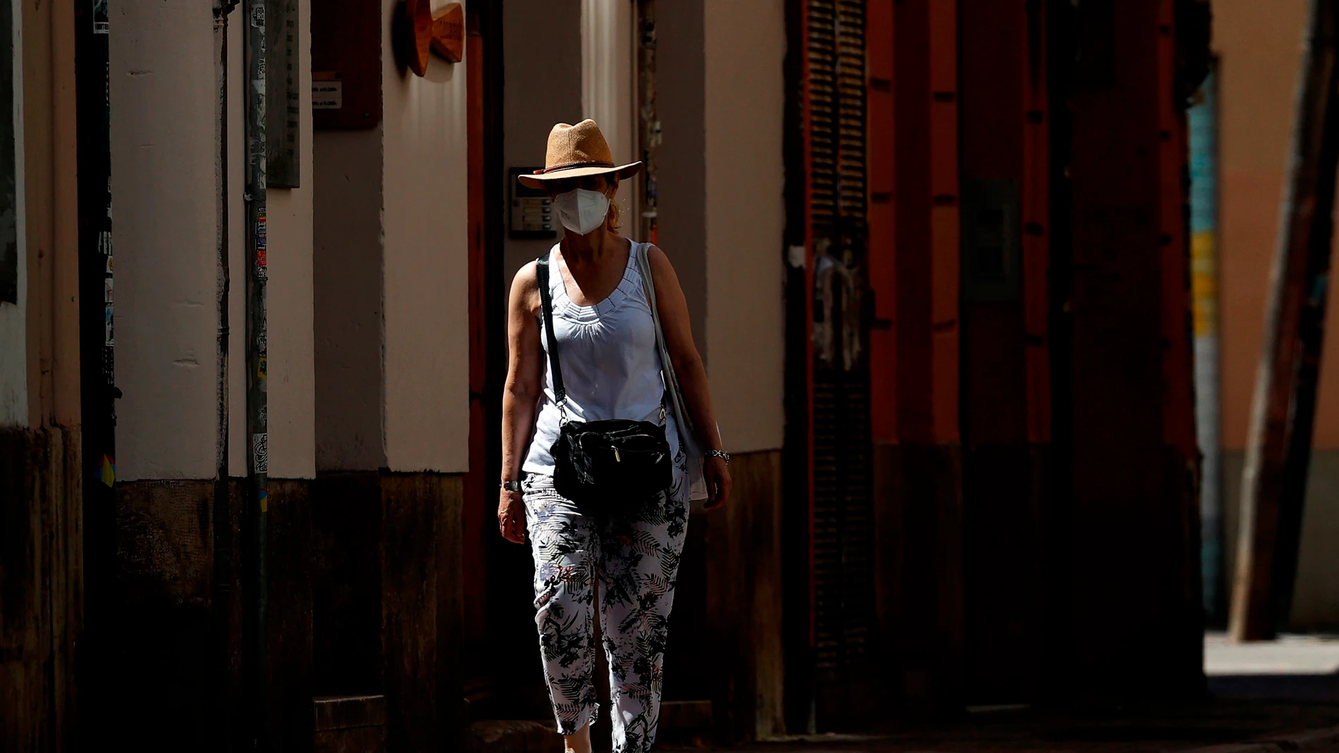 Una mujer pasea protegida con un sombrero y una mascarilla por una calle del casco antiguo de Valéncia