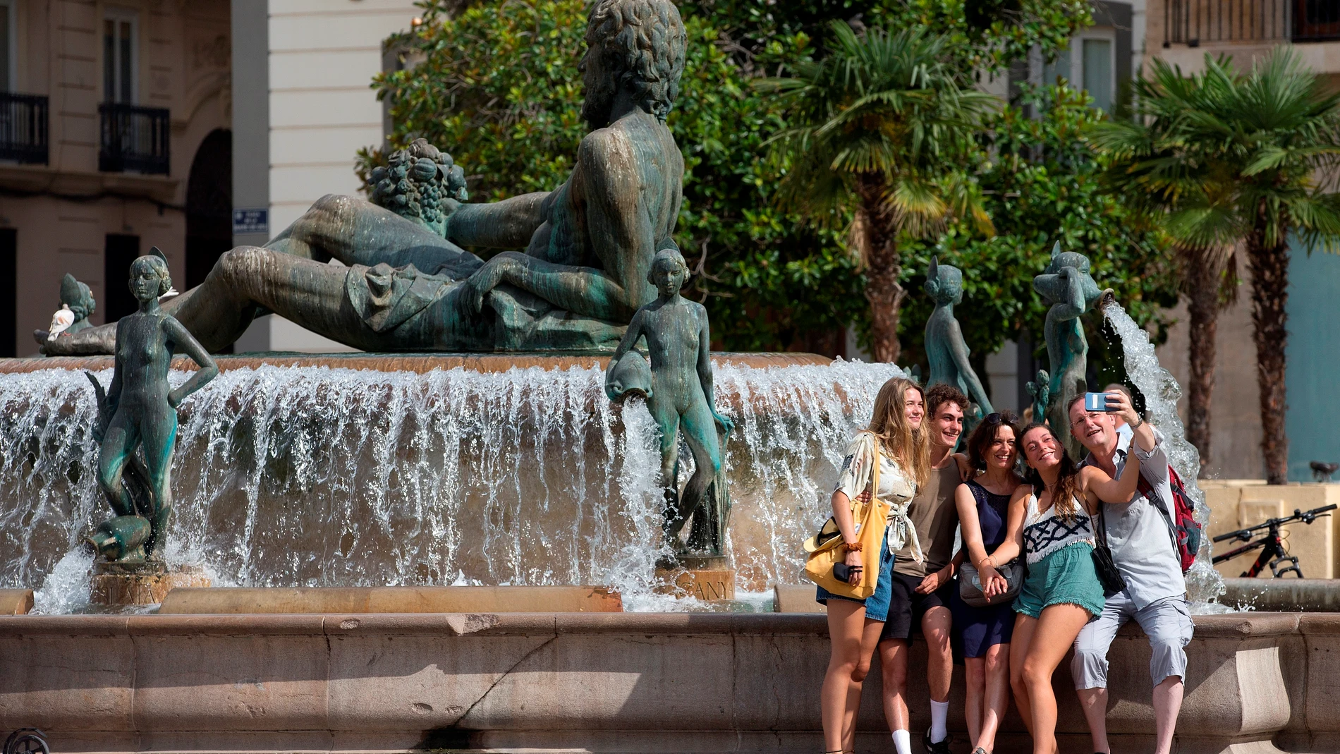 Un grupo de turistas se hace una fotografía junto a la fuente en la plaza de la Virgen de Valencia.