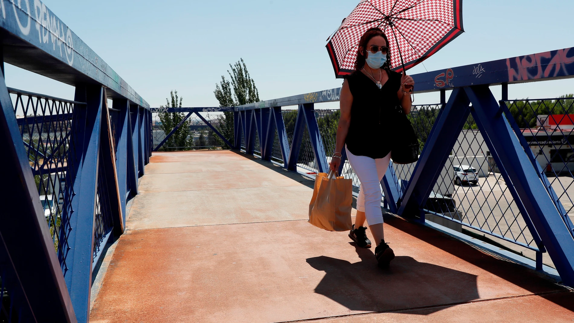 Una mujer se protege del sol con un paraguas mientras cruza por una pasarela, este viernes en Madrid.