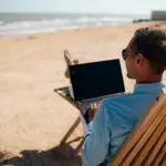 Young attractive man relaxing at the beach with laptop computer. back view.