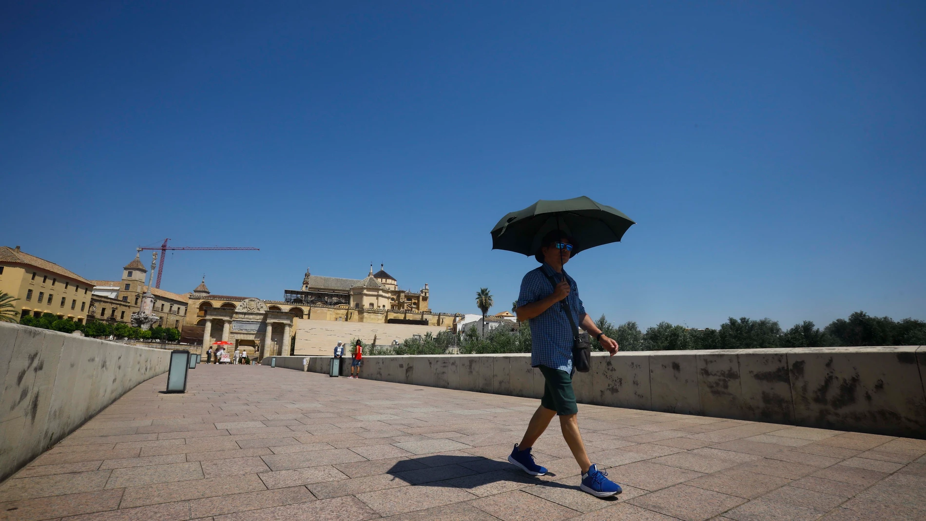 Un turista se resguarda del sol bajo un paraguas mientras camina por el Puente Romano de Córdoba