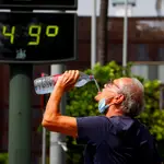 Un turista se refresca en el centro de Córdoba junto a un termómetro que, recalentado por su exposición al sol, marca 49 grados