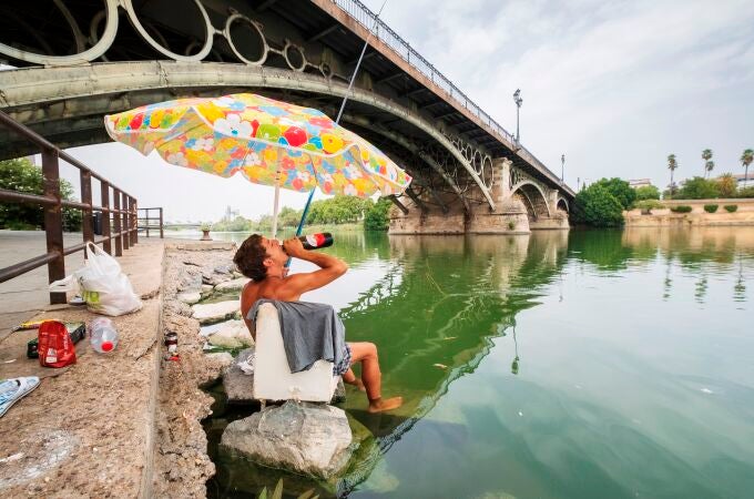Un joven se refresca mientras pesca en la dársena del Guadalquivir de Sevilla durante una ola de calor el pasado verano