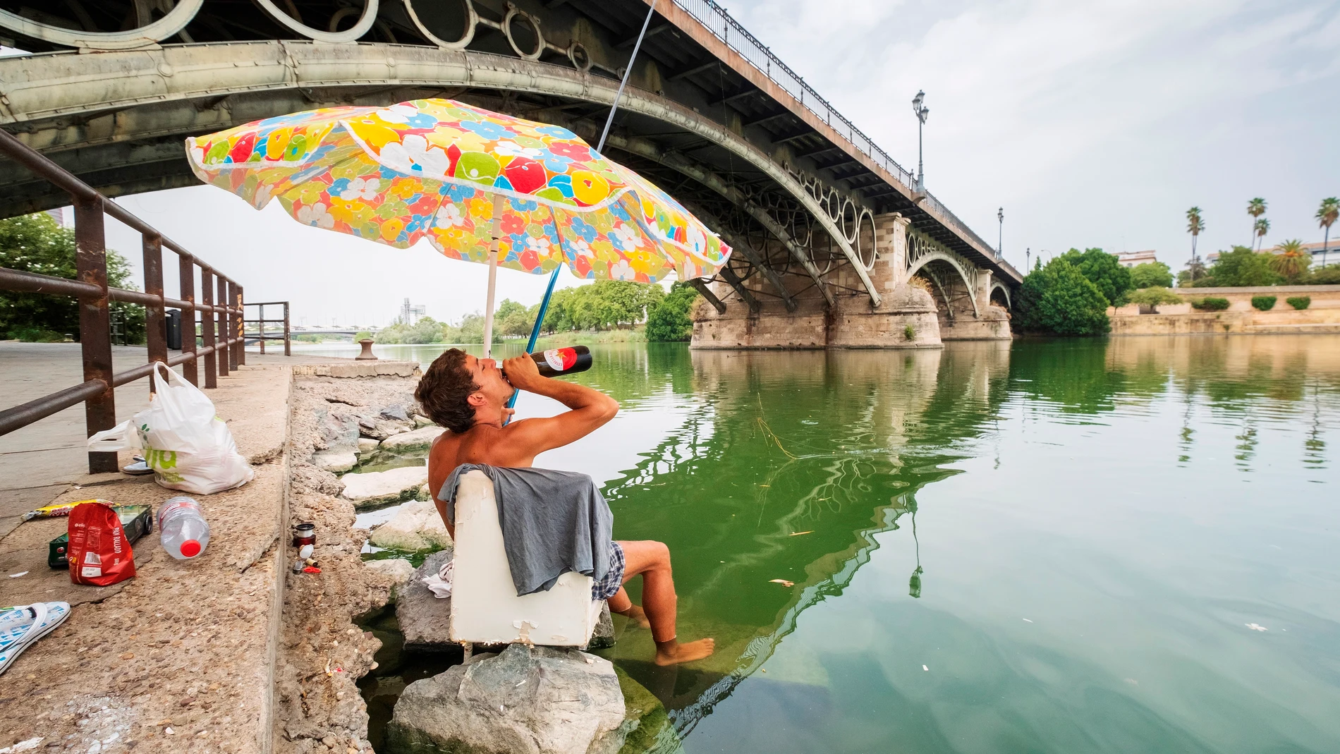 Un joven se refresca mientras pesca en la dársena del Guadalquivir de Sevilla durante una ola de calor el pasado verano
