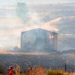 Un bombero pasa este domingo junto a una edificación calcinada por el incendio declarado ayer en los municipios abulenses de Navalacruz y Cepeda de la Mora y La Parra. EFE/Raúl Sanchidrián