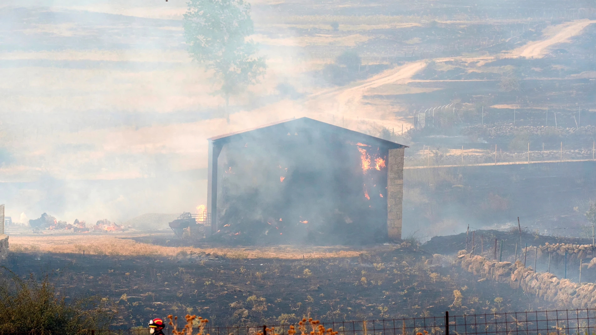 Un bombero pasa este domingo junto a una edificación calcinada por el incendio declarado ayer en los municipios abulenses de Navalacruz y Cepeda de la Mora y La Parra. EFE/Raúl Sanchidrián